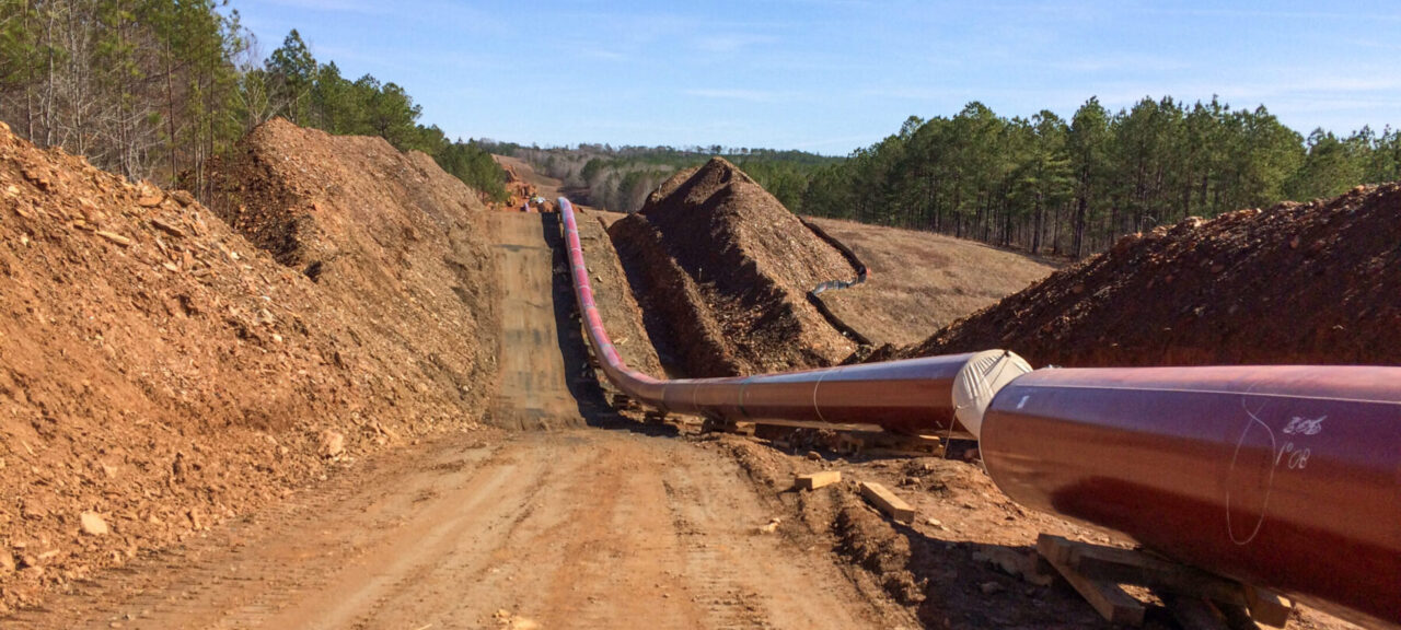 An above-ground natural gas pipeline is running parallel to the dirt even going up a hill.