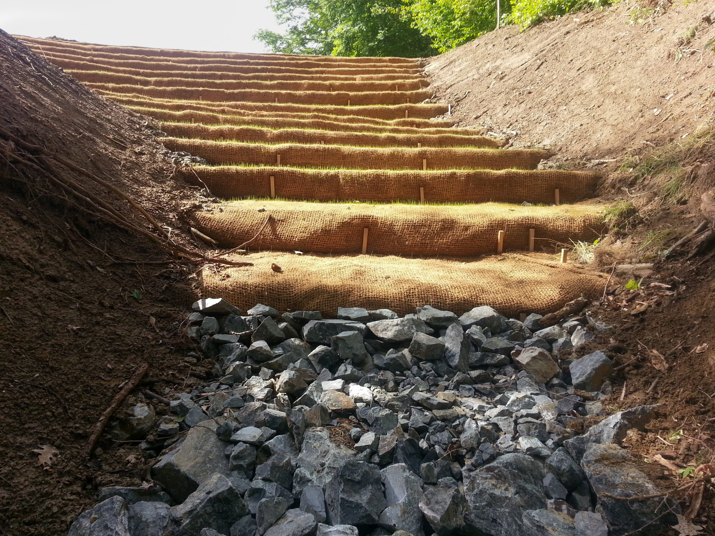 A stepped slope covered in burlap material with rock aggregate at the bottom.