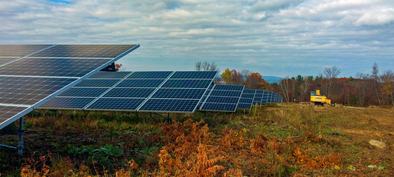 Low angle view of a solar panel array installed in a cleared field, with a construction vehicle in view.