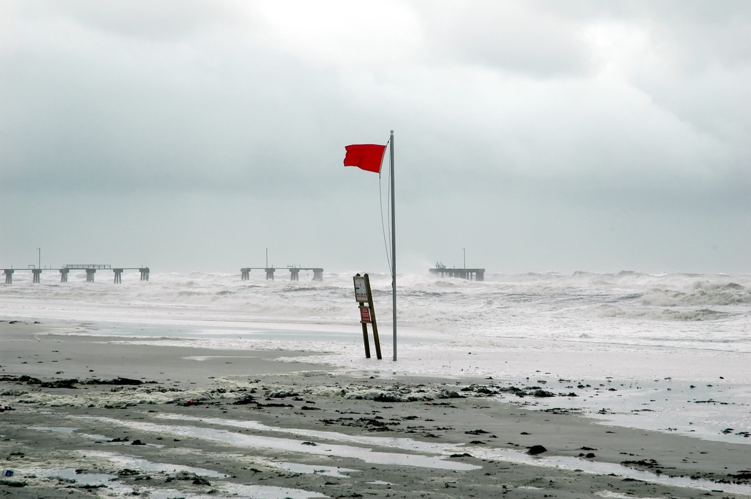 Hurricane with red warning flag and damaged pier in background.