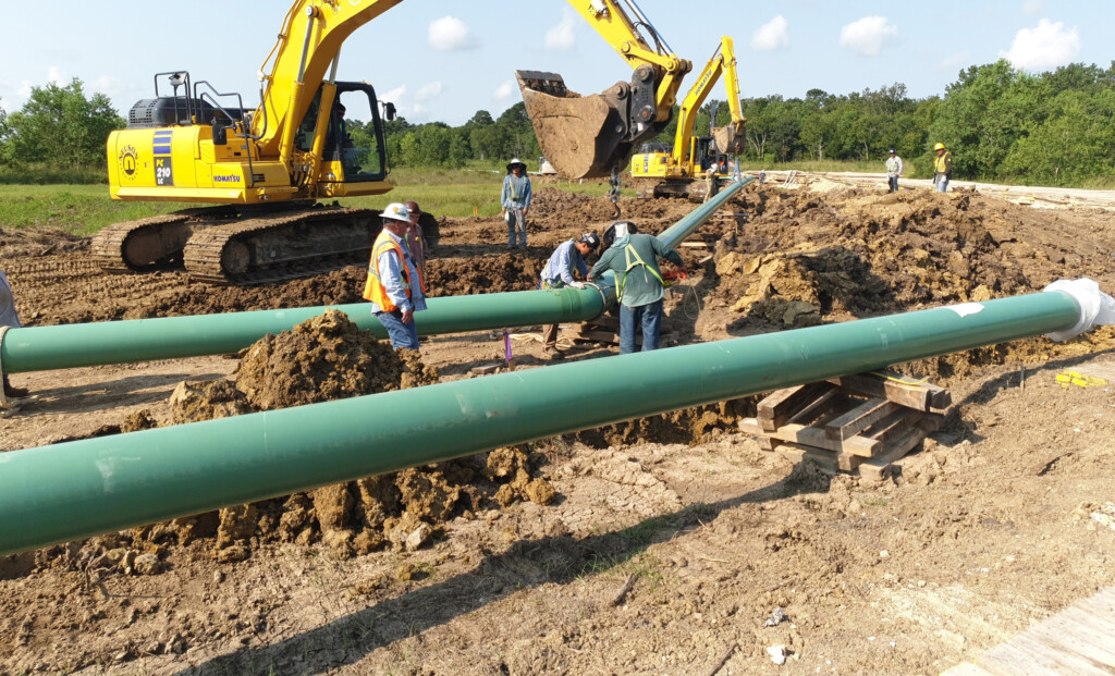 Contractors working on pipes with excavators in the background.