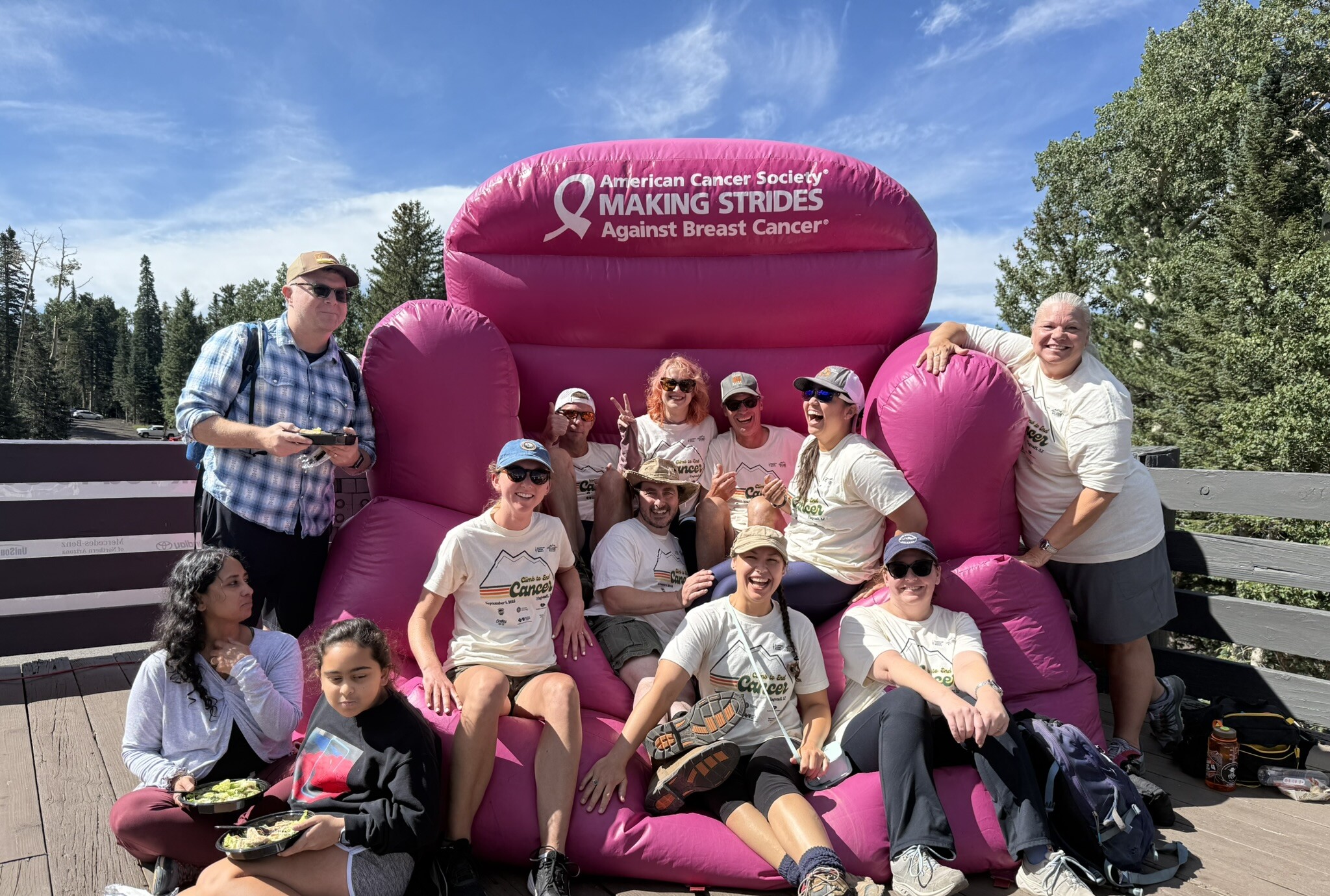 A group of people laying on a large inflatable pink seat that has the words "American Cancer Society Making strides against Breast Cancer"