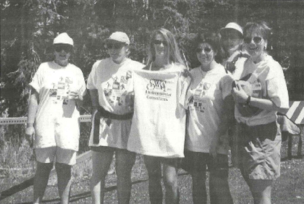 This team photo highlights Jean Ballagh on the far left with the first team she assembled in 1995. The image is in black and white and shows six team members standing next to each other while holding an SWCA shirt. 