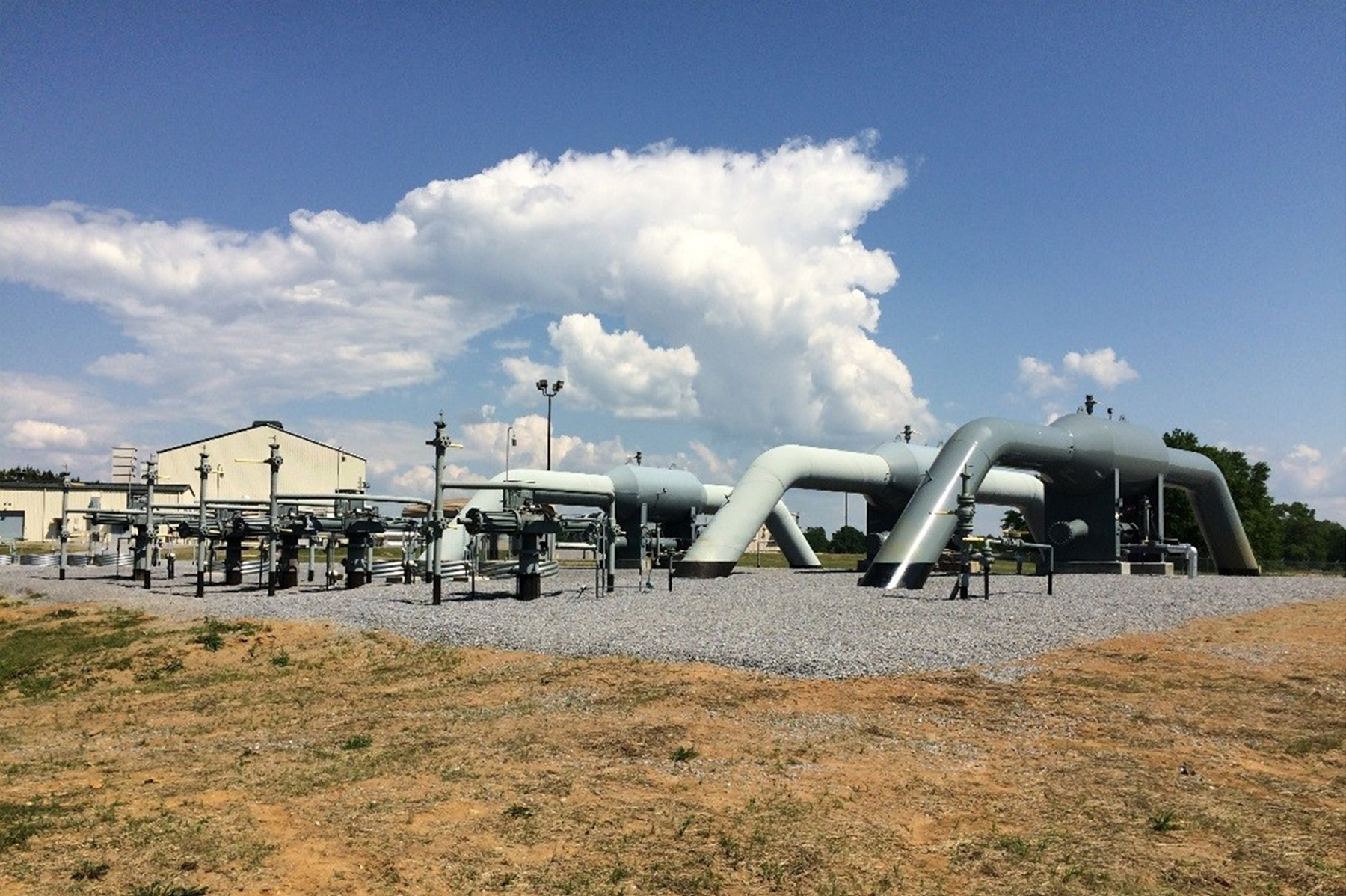 A Natural Gas Compression station is shown with some buildings and clouds in the background.