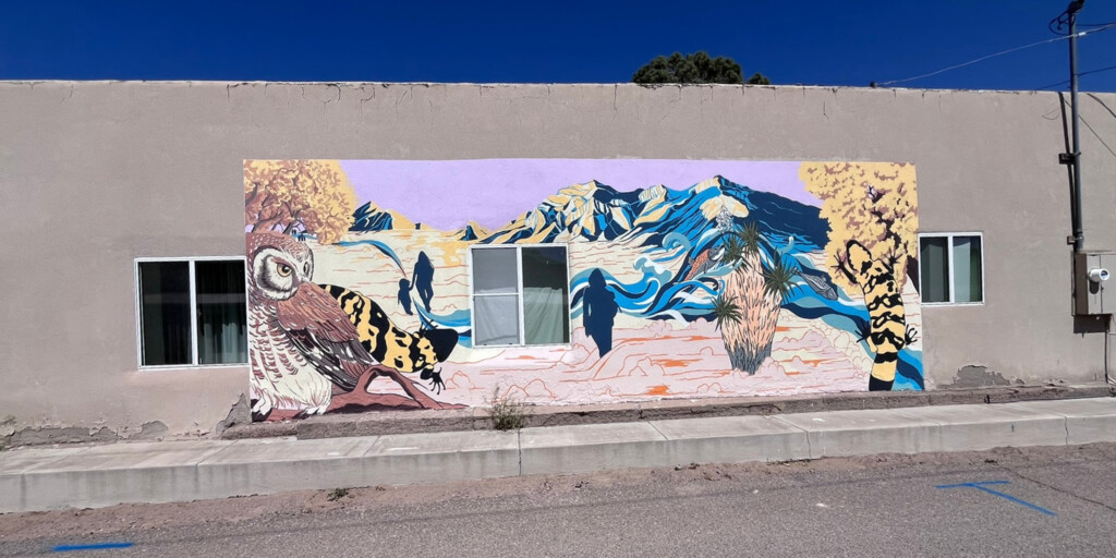 A mural on a wall showing an owl, a lizard, people and a mountain range.