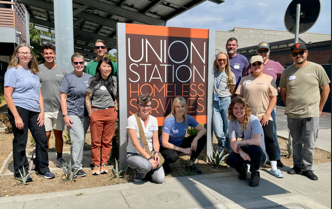 13 employees participated in preparing food for future hot meals and organizing boxes for grocery items to be given to individuals who suffer from food insecurity. These employees can be seen standing and kneeling in front of a Union Station Homeless Services sign. Andres Berdeja Annes Kim Antonio LaMadrid Jennie Stott Lauren Strong Liz Denniston Louise Parker Sarah Albertson Sheri Waldbauer Mike Crow Lisa DeLance Seth Dallman Brooke Langle