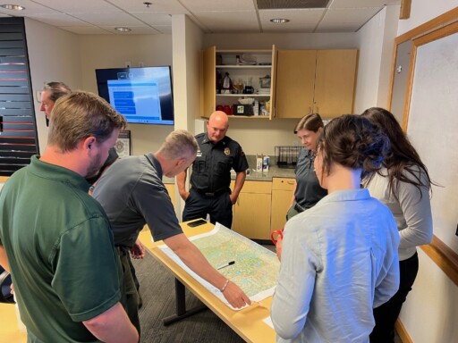 A group of people standing in a room surrounding a table with a map on it.