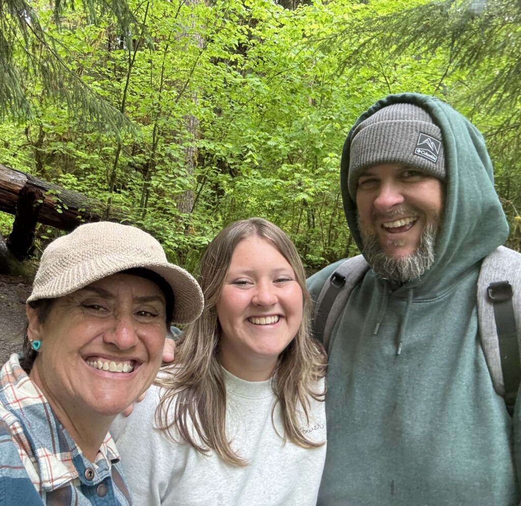 Lindsey Teunis standing with two other people outside with green plants behind them.