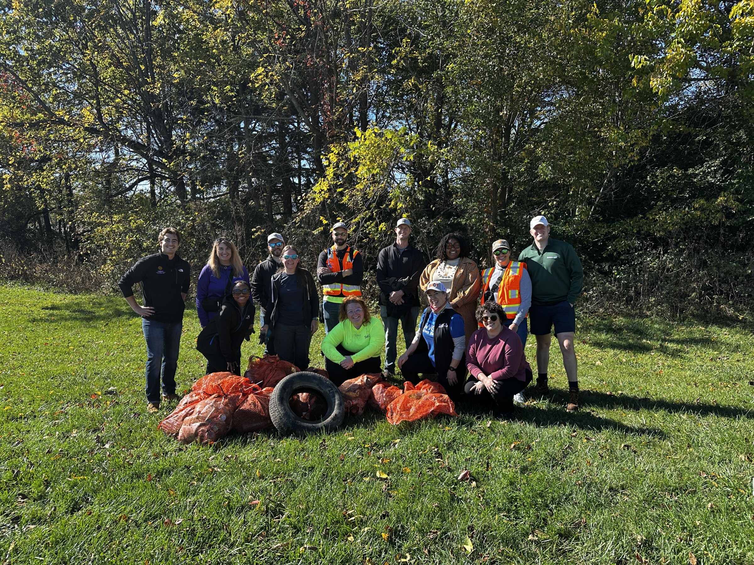 Several people posing in front of garbage bags and a tire from a clean up event.