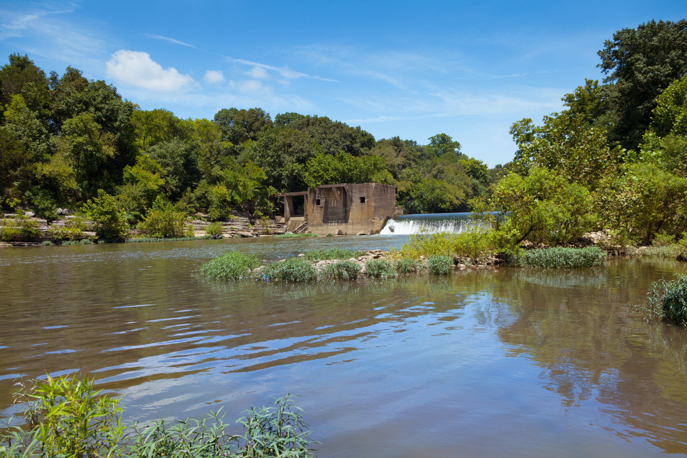 Lillard Mill Dam with water flowing towards a main body of water with trees surrounding the dam and water.