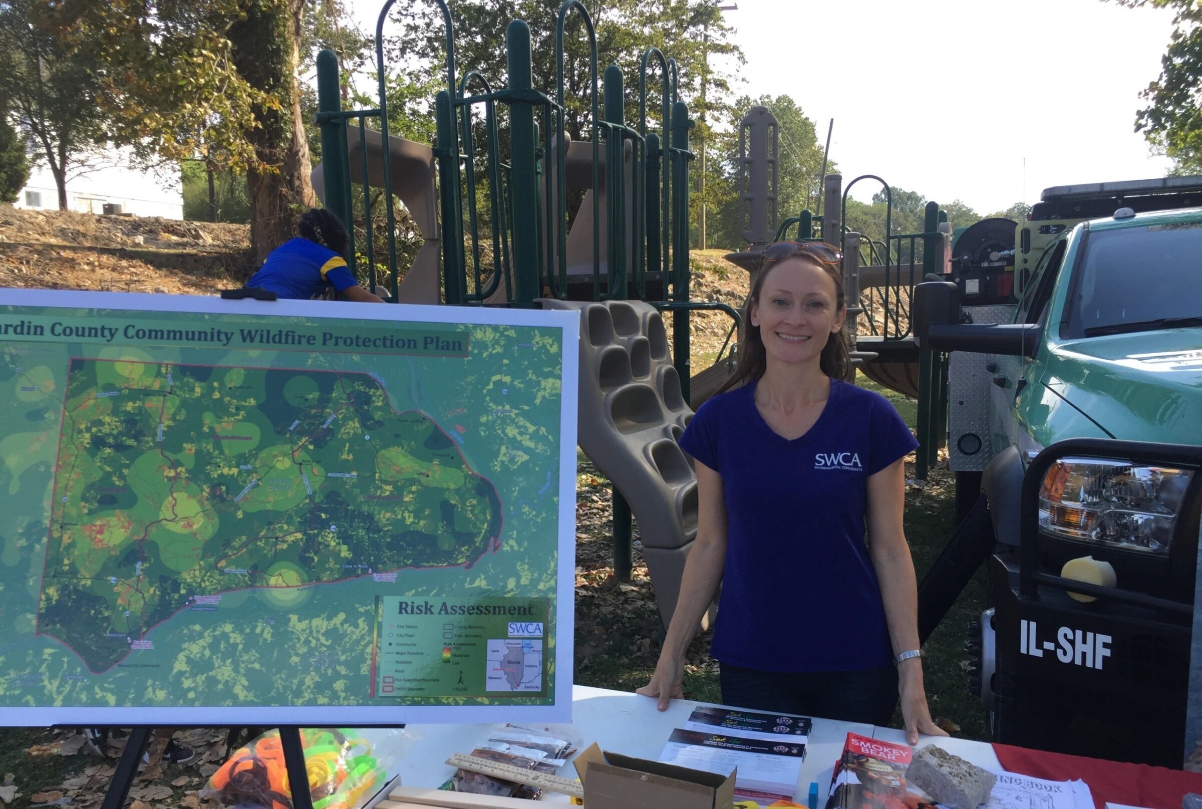 Victoria Amato standing in front of a playground and vehicle with a CWPP plan poster in front of her. 