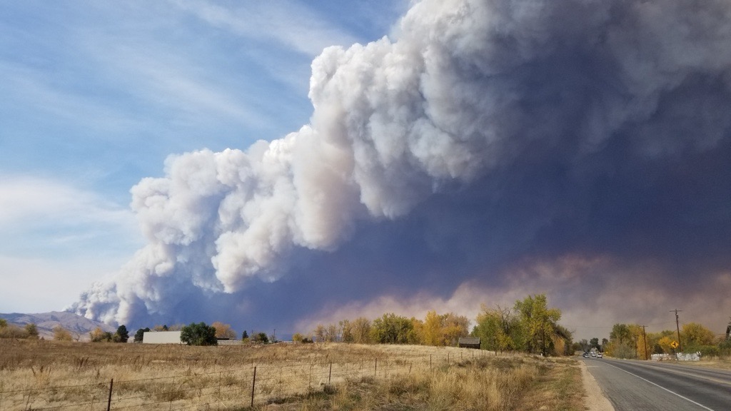A large plume of smoke is shown by a road, a field, and some scattered structures. 