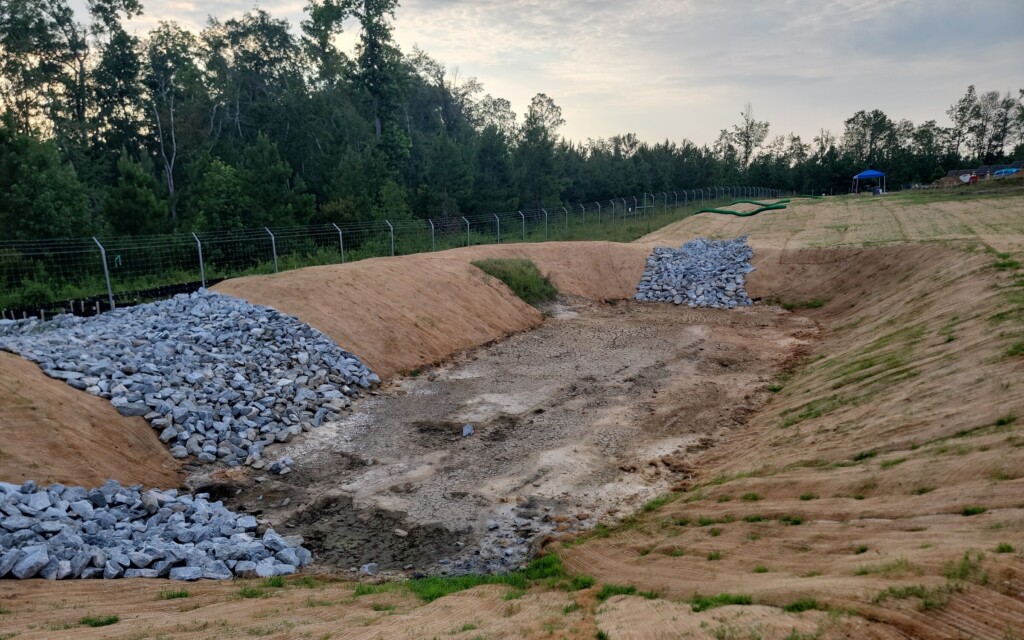 A retention pod is shown with rocks on the banks and erosion being shown on the sides. 