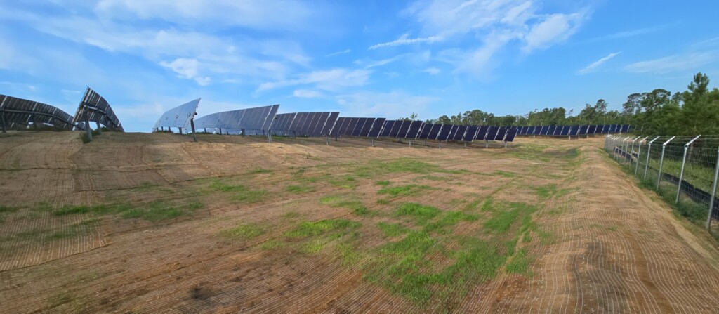Solar panels are seen with a dirt field next to it with some grass growing on it. 