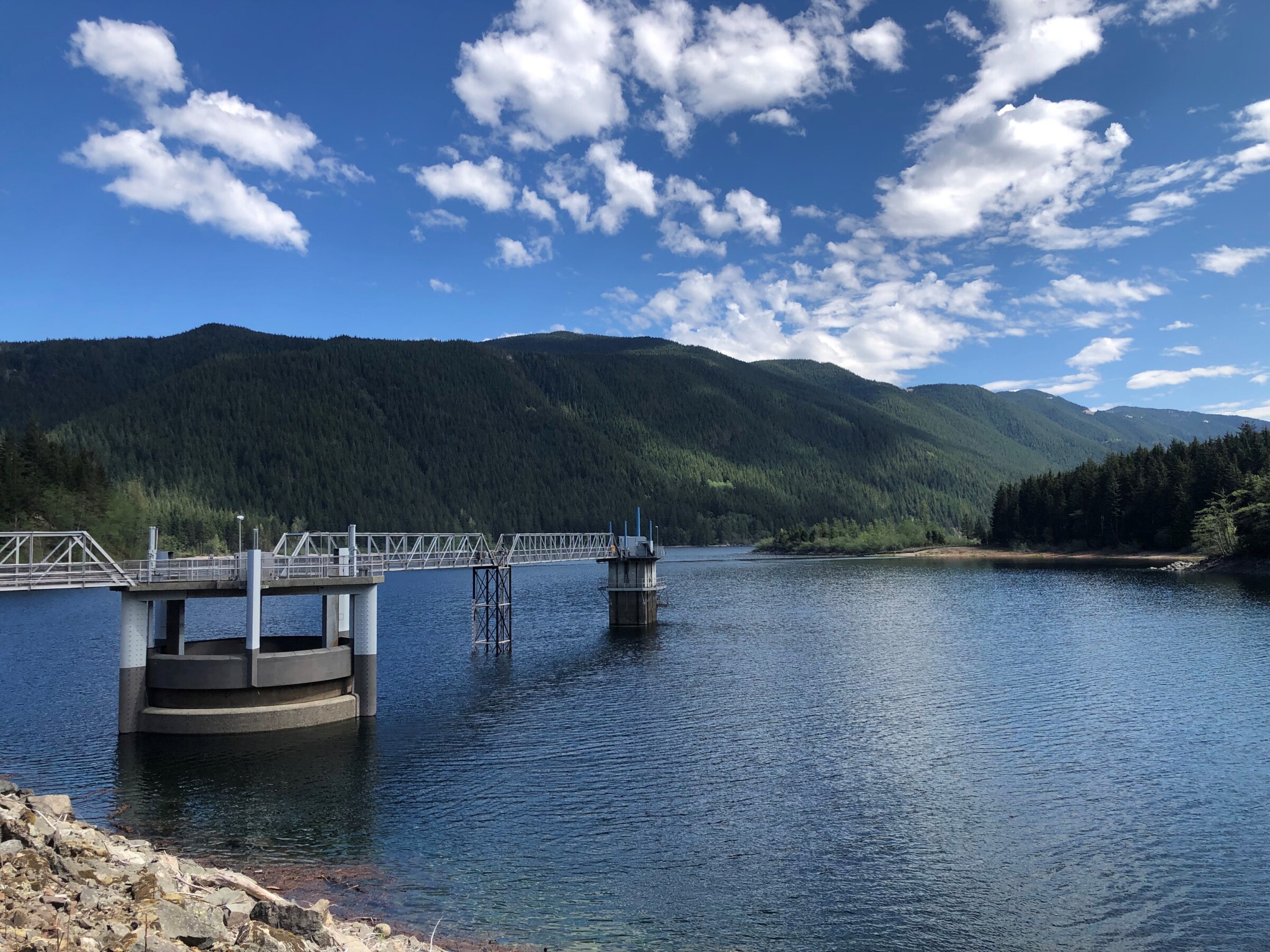 Intake structures shown on a large body of water with a hill covered in tree in the background.