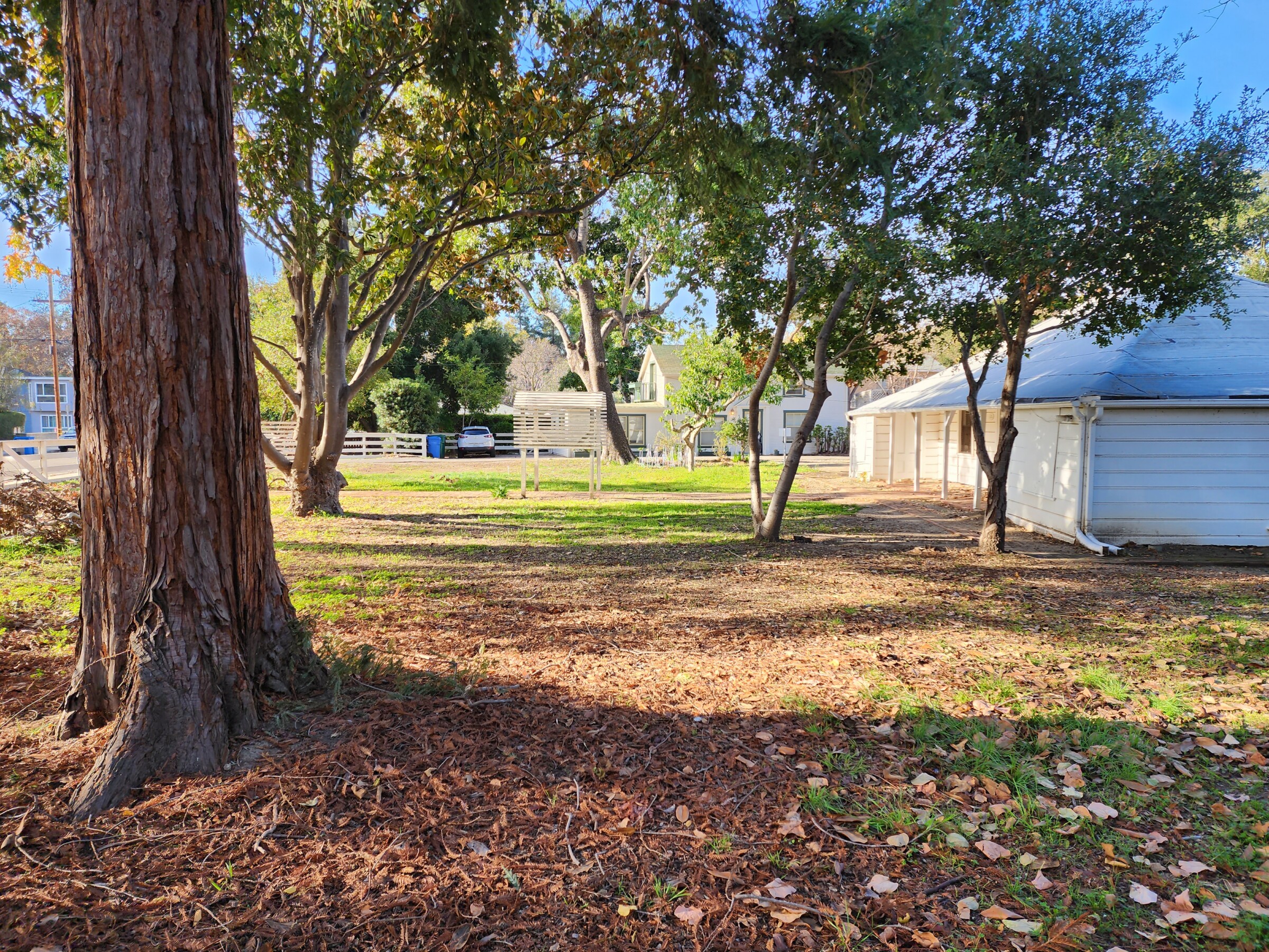 A view from the front corner of the property shows a large, tree-shaded setback between the street and the historic house.